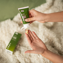 Load image into Gallery viewer, A woman's hands squeezing out a generous dollop of Yes OB oil based lubricant onto her fingers in front of a soft, cream coloured throw blanket