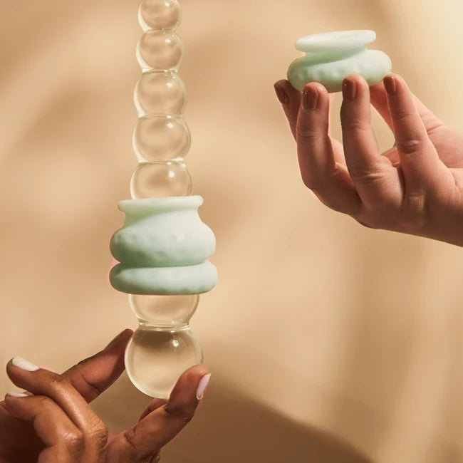 Two hands holding squishy Ohnut bumpers and demonstrating how they are used on a glass object.